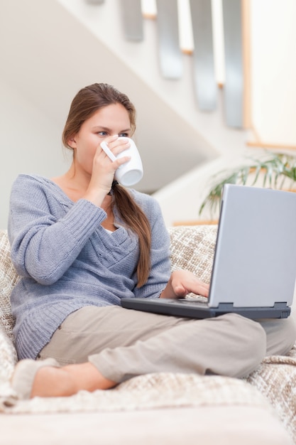 Porträt einer Frau, die einen Laptop beim Trinken einer Tasse Tee verwendet