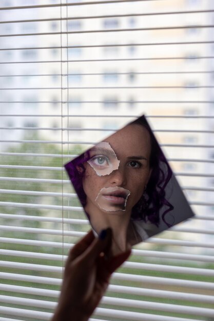 Foto porträt einer frau, die einen spiegel am fenster hält