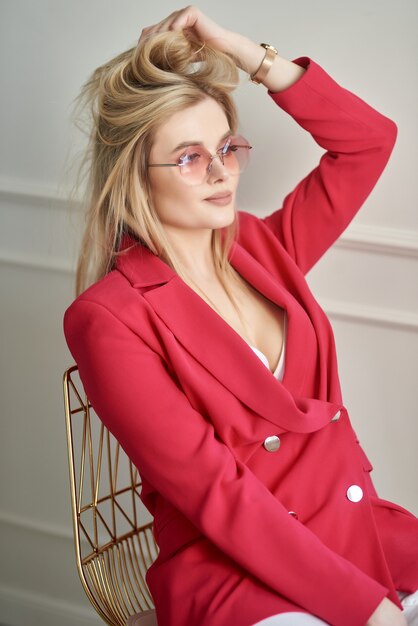 Porträt einer Frau, die in rosa Jacke und Brille auf einem Stuhl im Studio sitzt sitting