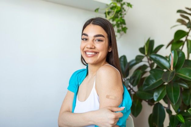 Foto porträt einer frau, die lächelt, nachdem sie einen impfstoff erhalten hat. frau, die ihren hemdärmel herunterhält und ihren arm mit verband zeigt, nachdem sie die impfung erhalten hat.