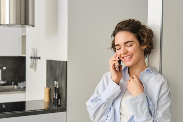 Porträt einer Frau, die mit dem Mobiltelefon spricht und lächelt, während sie zu Hause Zeit mit Telefon verbringt