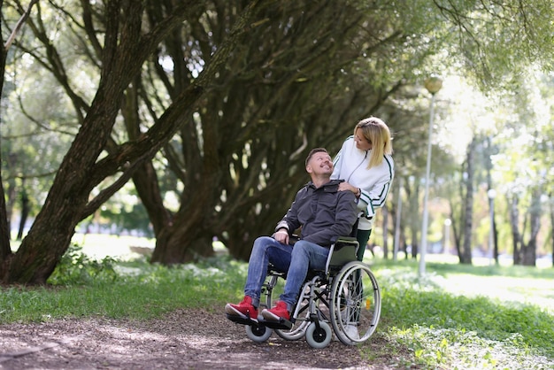 Porträt einer Frau, die mit einem behinderten Mann im Rollstuhl im Park spazieren geht Paar in Liebe Behinderung und