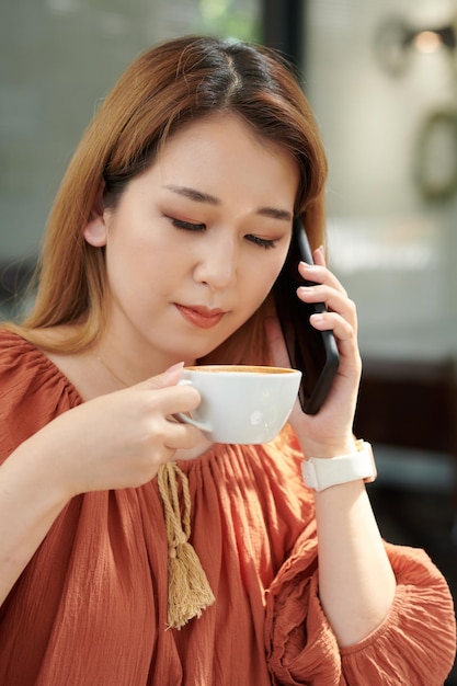 Porträt einer Frau, die Morgenkaffee trinkt und telefoniert