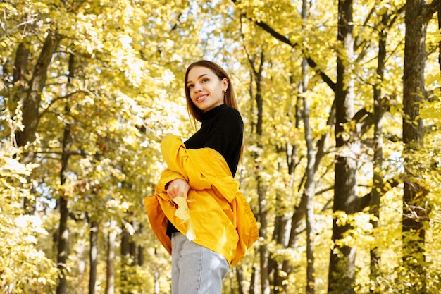 Porträt einer Frau, die vor dem Hintergrund eines herbstlichen gelben Waldes lächelt