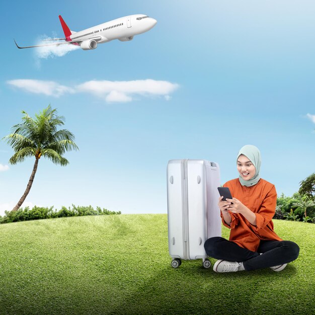 Porträt einer Frau im Hijab mit einem Koffer, die ein Handy benutzt, während sie mit einem fliegenden Flugzeug reist