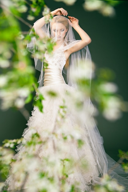 Porträt einer Frau im Hochzeitskleid hinter den grünen Zweigen mit Blumen