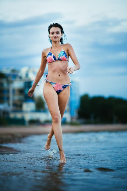 Foto porträt einer frau in bikini, die im meer gegen den himmel geht