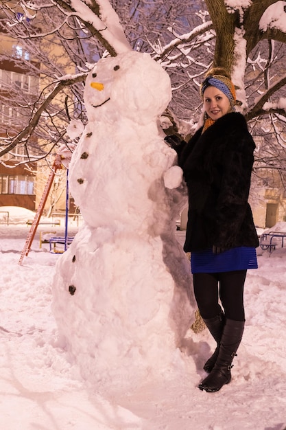 Porträt einer Frau in einem schwarzen Pelzmantel in der Nähe des großen Schneemanns im Hof