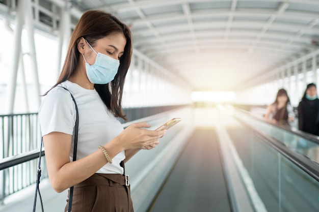 Porträt einer Frau in einer medizinischen Maske, die mit ihrem Smartphone draußen plaudert