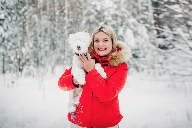 Porträt einer Frau in einer roten Jacke mit einem Hund in einem kalten Winterwald.