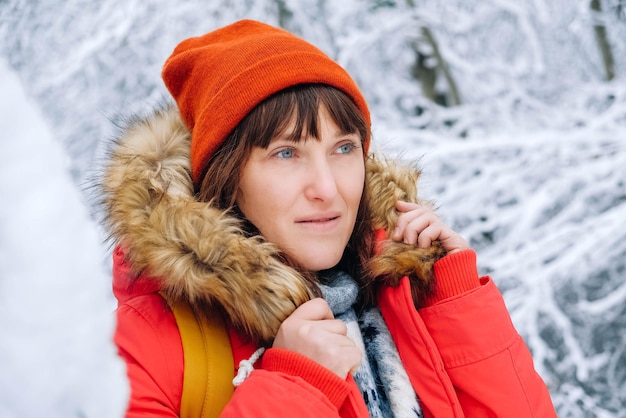 Porträt einer Frau in einer roten warmen Jacke und einem Hut in einem verschneiten Winterwald