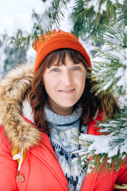 Porträt einer Frau in einer roten warmen Jacke und einem Hut in einem verschneiten Winterwald
