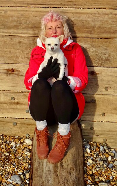 Foto porträt einer frau mit einem hund, der an einer holzmauer sitzt