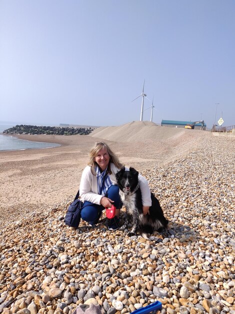 Foto porträt einer frau mit einem hund, die am strand sitzt