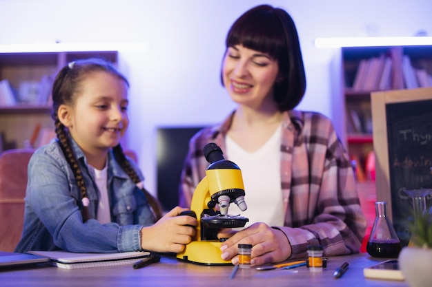 Porträt einer Frau mit einem Mädchen, das an einem Tisch mit einem Elektronenmikroskop sitzt