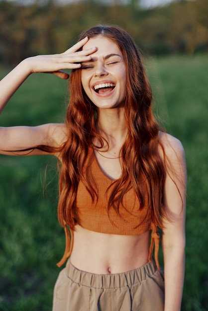 Porträt einer Frau mit einem schönen Lächeln in der sommergrünen Natur vor dem Gras, die auf die untergehende Sonne blickt. Das Konzept von Gesundheit und Schönheit