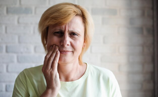 Porträt einer Frau mittleren Alters, die den Mund mit der Hand berührt, mit schmerzhaftem Gesichtsausdruck wegen starker Zahnschmerzen oder Zahnerkrankungen an den Zähnen. Traurige reife Frau mit Schmerzen aufgrund von Zahnschmerzen