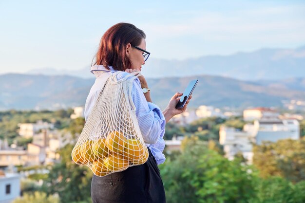 Porträt einer Frau mittleren Alters mit Smartphone und trendigem Orangengitter im Freien