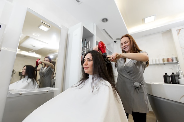 Porträt einer Friseurin, die mit einem Kunden in einem Schönheitssalon arbeitet. Friseur trocknet nasses Haarmädchen mit einem Fön