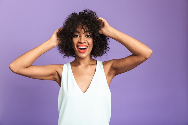 Porträt einer fröhlichen afrikanischen Frau, die ein Kleid trägt, das isoliert über violettem Hintergrund steht