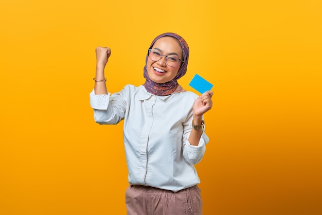 Porträt einer fröhlichen asiatischen Frau, die Glück feiert und eine leere Karte auf gelbem Hintergrund hält