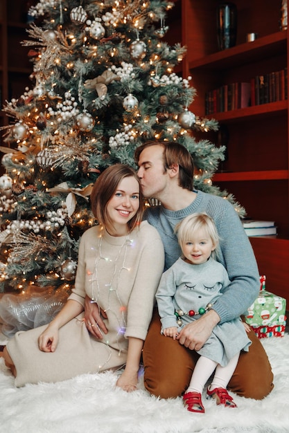 Porträt einer fröhlichen Familie, die am Weihnachtsbaum sitzt