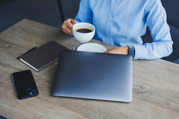 Porträt einer fröhlichen Frau mit klassischer Brille, die in der Freizeit im Café mit Kaffee lächelt positive europäische Frau im blauen Hemdschreibtisch mit Laptop-Fernarbeit