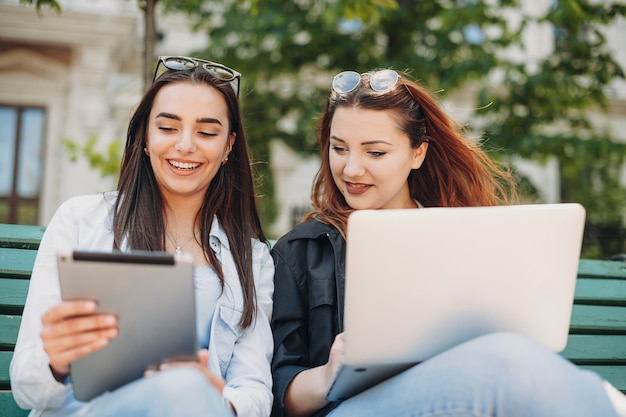 Porträt einer fröhlichen Frau mit langen dunklen Haaren, die lachen, während sie eine Tablette halten, während ihre Freundin den Bildschirm der Tablette lächelnd betrachtet.