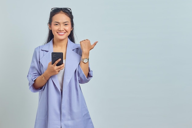 Porträt einer fröhlichen jungen Asiatin, die Handy hält und Kopienraum isoliert auf weißem Hintergrund zeigt