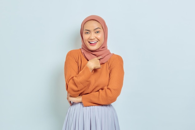 Porträt einer fröhlichen jungen asiatischen Frau, die stolz auf sich selbst zeigt, isoliert auf weißem Hintergrund Muslimisches Lifestyle-Konzept