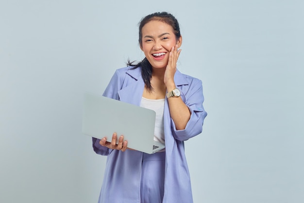 Porträt einer fröhlichen jungen asiatischen Frau mit Laptop und Kinn mit Handflächen isoliert auf weißem Hintergrund