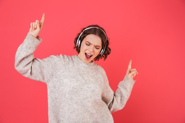 Porträt einer fröhlichen jungen Frau, die isoliert über Rosa steht und Musik mit Kopfhörern hört, tanzt