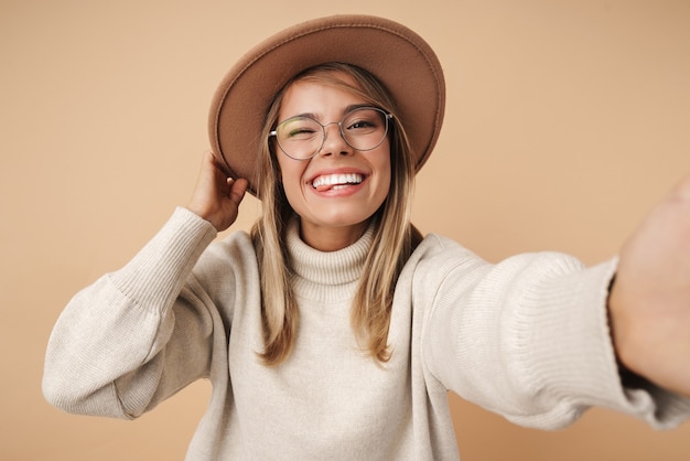 Porträt einer fröhlichen jungen Frau mit Hut, die zwinkert und ein Selfie-Foto macht