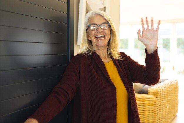 Foto porträt einer fröhlichen kaukasischen seniorin, die lacht und mit der hand winkt, während sie am eingang begrüßt