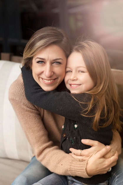 Porträt einer fröhlichen Mutter, die mit ihrer Tochter auf dem Sofa sitzt
