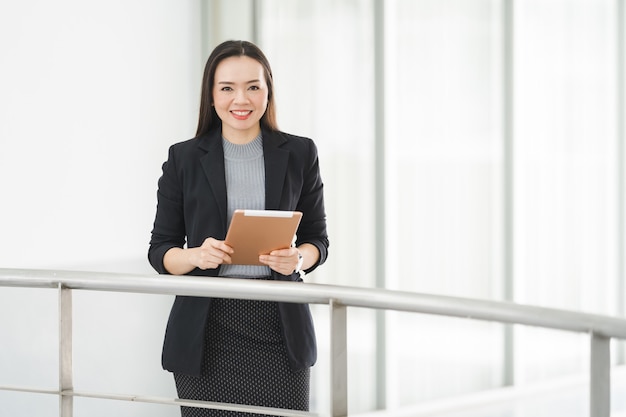 Porträt einer fröhlichen, selbstbewussten asiatischen Geschäftsfrau in einem Business-Anzug, der ein weißes Tablett im Geschäftsgebäude verwendet. Geschäft Stockfotos