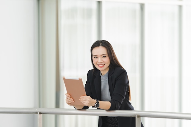 Porträt einer fröhlichen, selbstbewussten asiatischen Geschäftsfrau in einem Business-Anzug, der ein weißes Tablett im Geschäftsgebäude verwendet. Geschäft Stockfotos