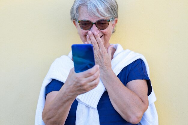 Porträt einer fröhlichen Seniorin, die ein Smartphone hält und lacht