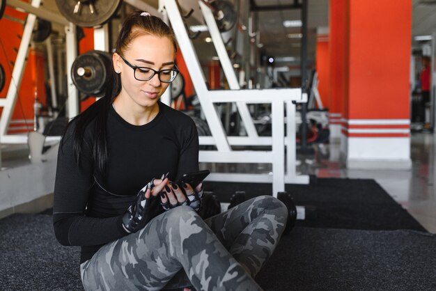 Porträt einer fröhlichen Sportfrau, die Smartphone im Fitnessstudio verwendet