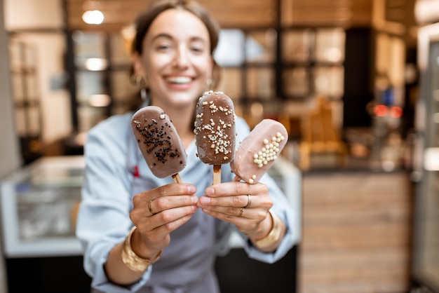 Porträt einer fröhlichen weiblichen Verkäuferin mit Schokoladen-Eis auf einem Stock im Laden