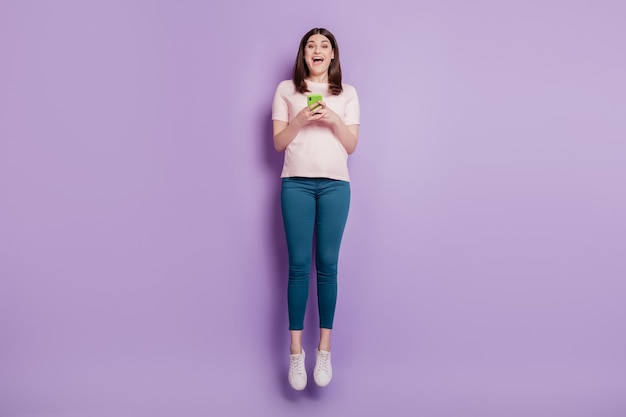 Porträt einer funky sorglosen, energiegeladenen Dame mit Handy-Sprung viel Spaß auf violettem Hintergrund