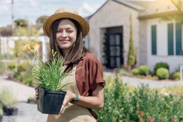 Porträt einer Gärtnerin, die eine mehrjährige Pflanze in den Händen hält und in der Nähe des Gartenhauses arbeitet