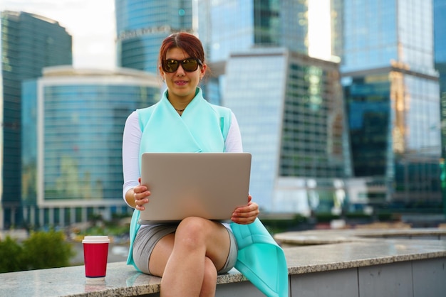 Porträt einer Geschäftsfrau, die im Freien mit Laptop und einer Tasse Kaffee sitzt