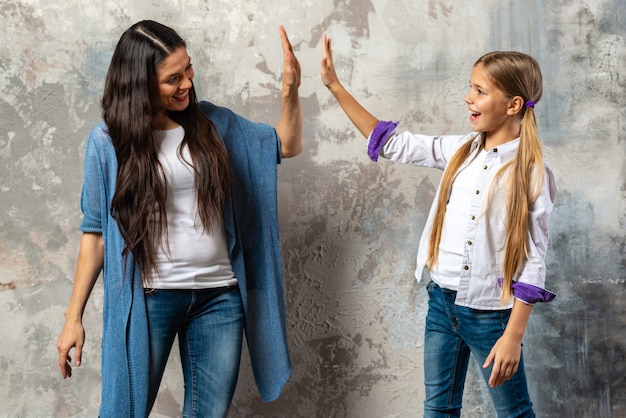 Porträt einer gladden Mutter und der Tochter, die Hoch fünf über grauem Hintergrund geben