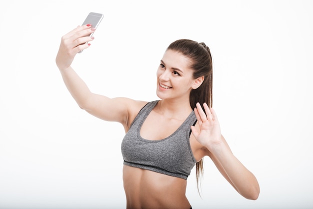 Porträt einer glücklich lächelnden Fitnessfrau, die isoliert auf ihr Handy winkt