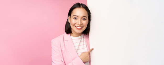 Porträt einer glücklich lächelnden japanischen Unternehmensfrau, die mit dem Finger auf ein Brett zeigt, das etw auf leerem SP zeigt