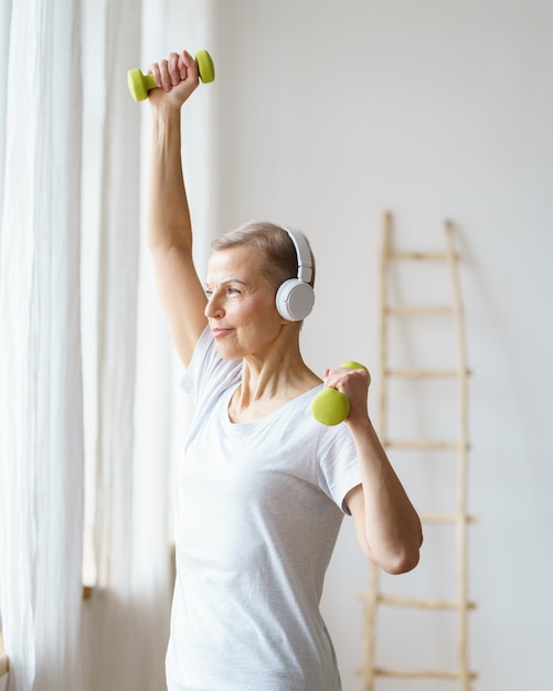 Porträt einer glücklichen älteren Frau, die zu Hause Fitnessübungen mit Hanteln macht