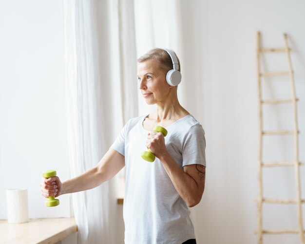 Porträt einer glücklichen älteren Frau, die zu Hause Fitnessübungen mit Hanteln macht