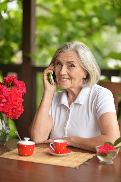 Porträt einer glücklichen alten Frau, die beim Kaffeetrinken mit dem Smartphone spricht