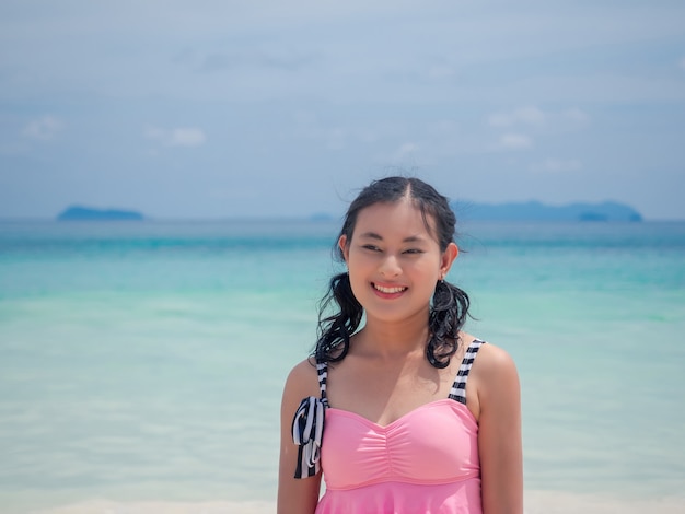 Porträt einer glücklichen asiatischen Frau im Badeanzug und nassem Haar am blauen Meeresstrand am hellen Tag